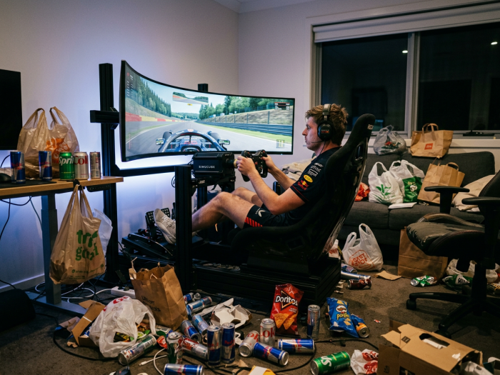 Person using a sim racing setup with curved screen surrounded by snack and drink waste