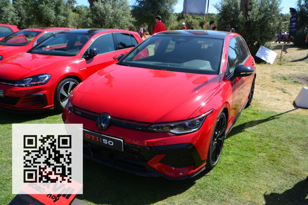 A red Volkswagen GTI car with a sleek design, parked on grass, with other red vehicles in the background and a QR code in the foreground.