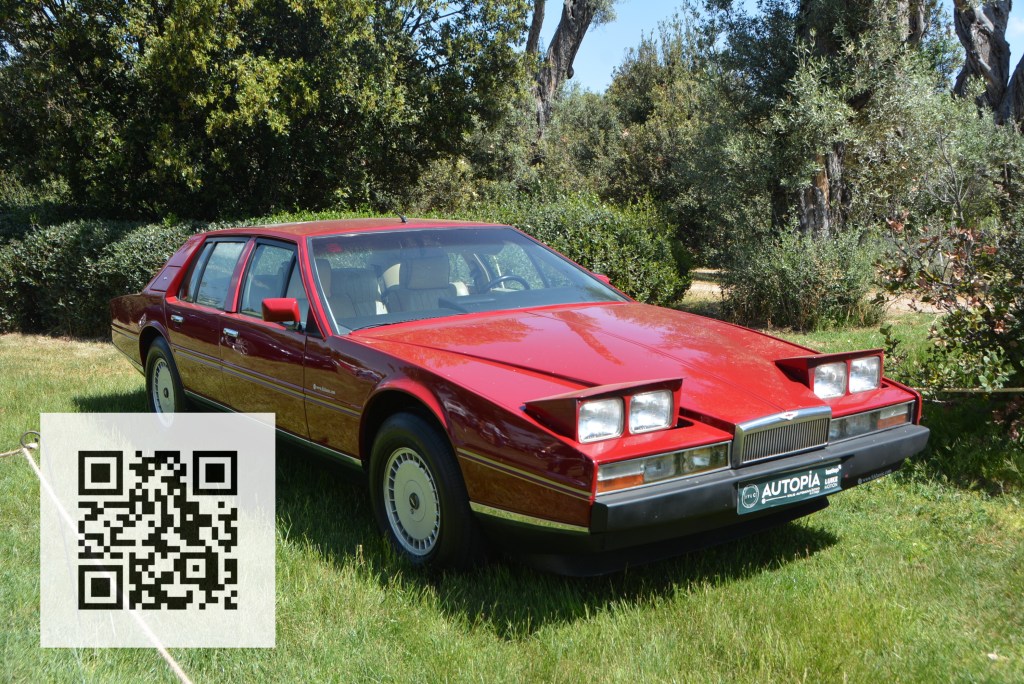 A shiny red luxury car parked on a grassy area, surrounded by trees, with a QR code displayed in the corner.