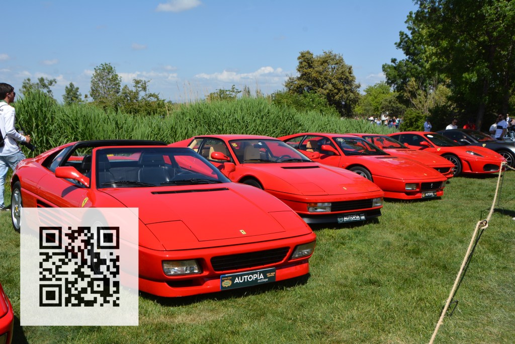 A lineup of red Ferrari sports cars displayed on a grassy area, featuring several models including convertibles and coupes, with a person standing nearby and a QR code in the foreground.