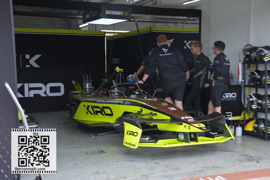 A racing car in a garage with team members working on it, showcasing the Kiro and Cupra branding.